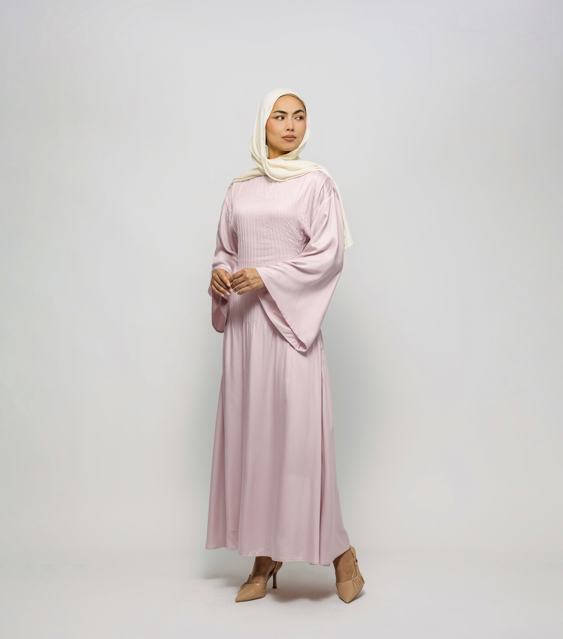 Woman wearing a light pink dress and hijab on a white background