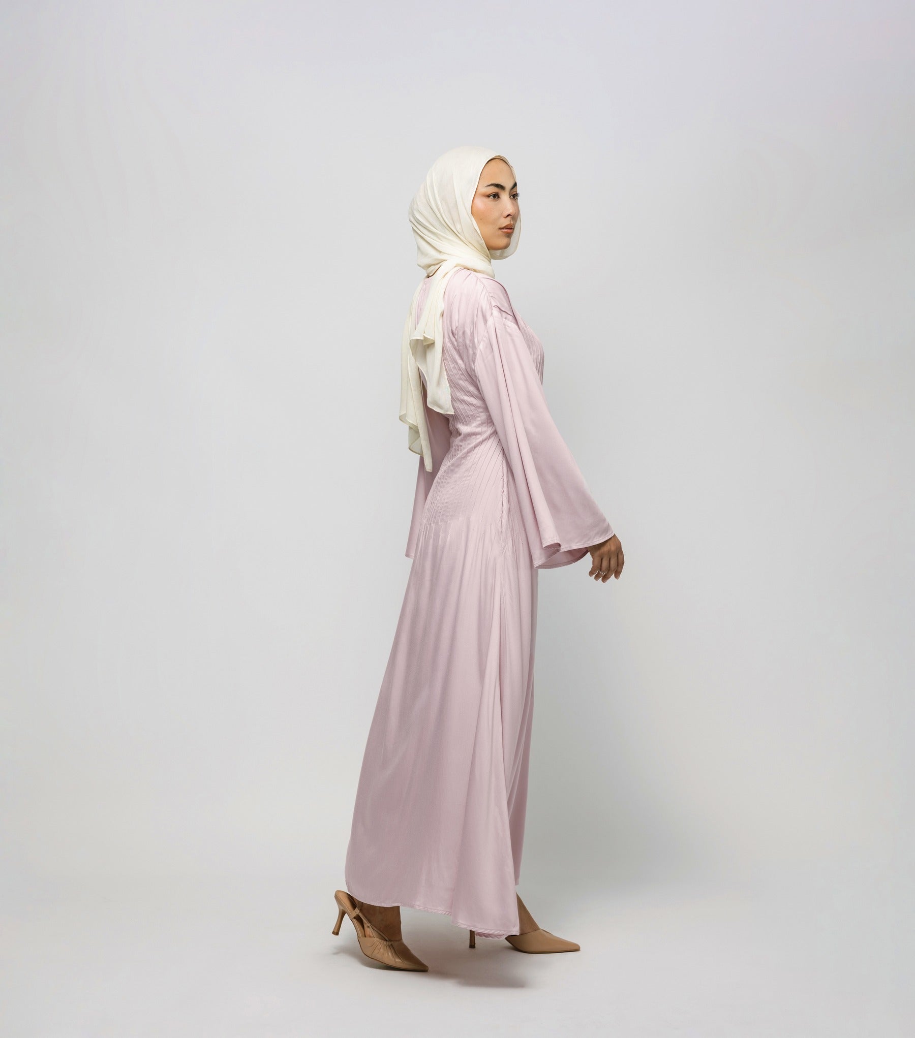 Woman wearing a light pink dress and hijab on a white background