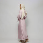Woman wearing a light pink dress and beige hijab against a white background