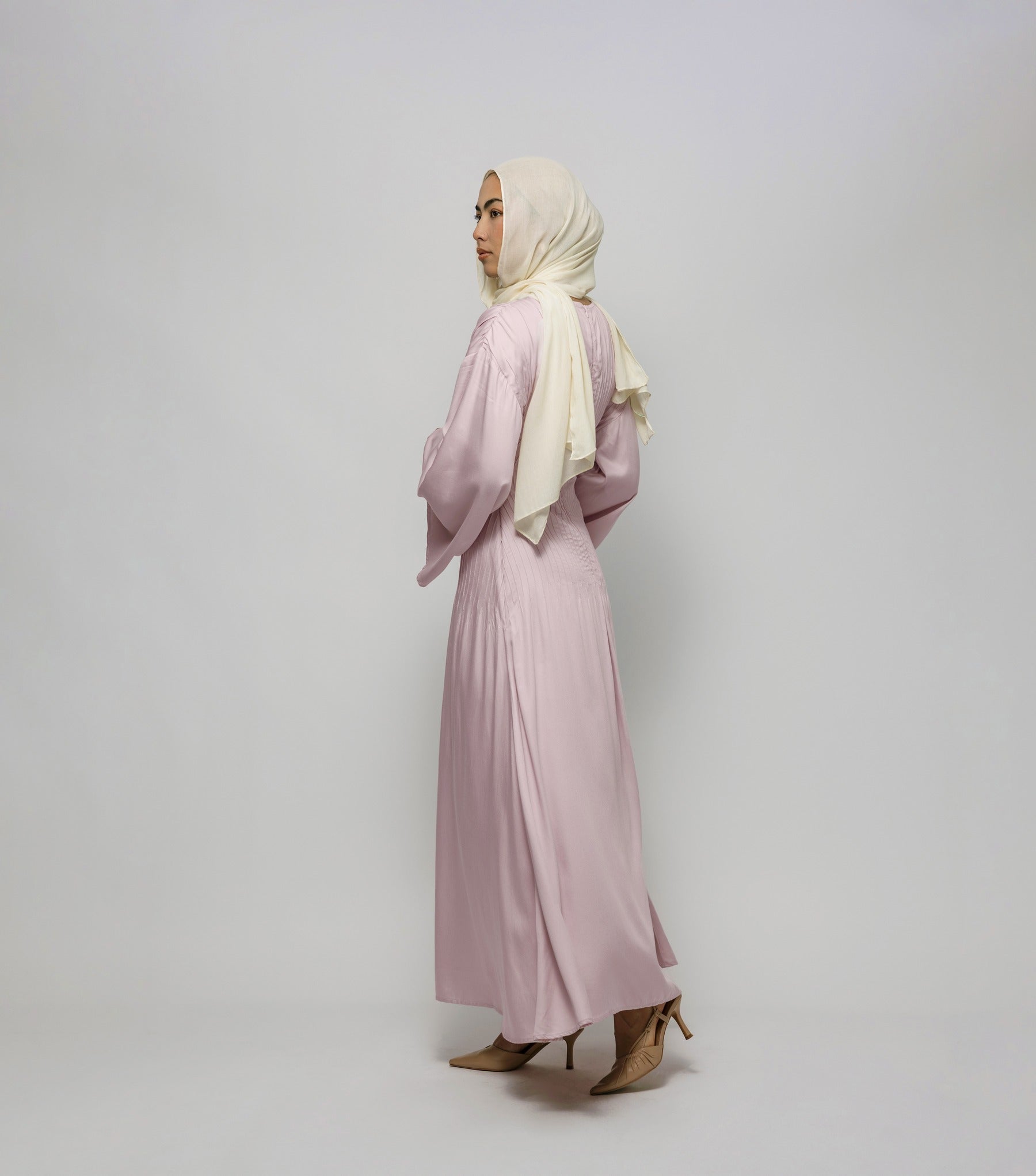 Woman wearing a light pink dress and beige hijab against a white background