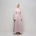 Woman wearing a long pink dress and hijab on a white background