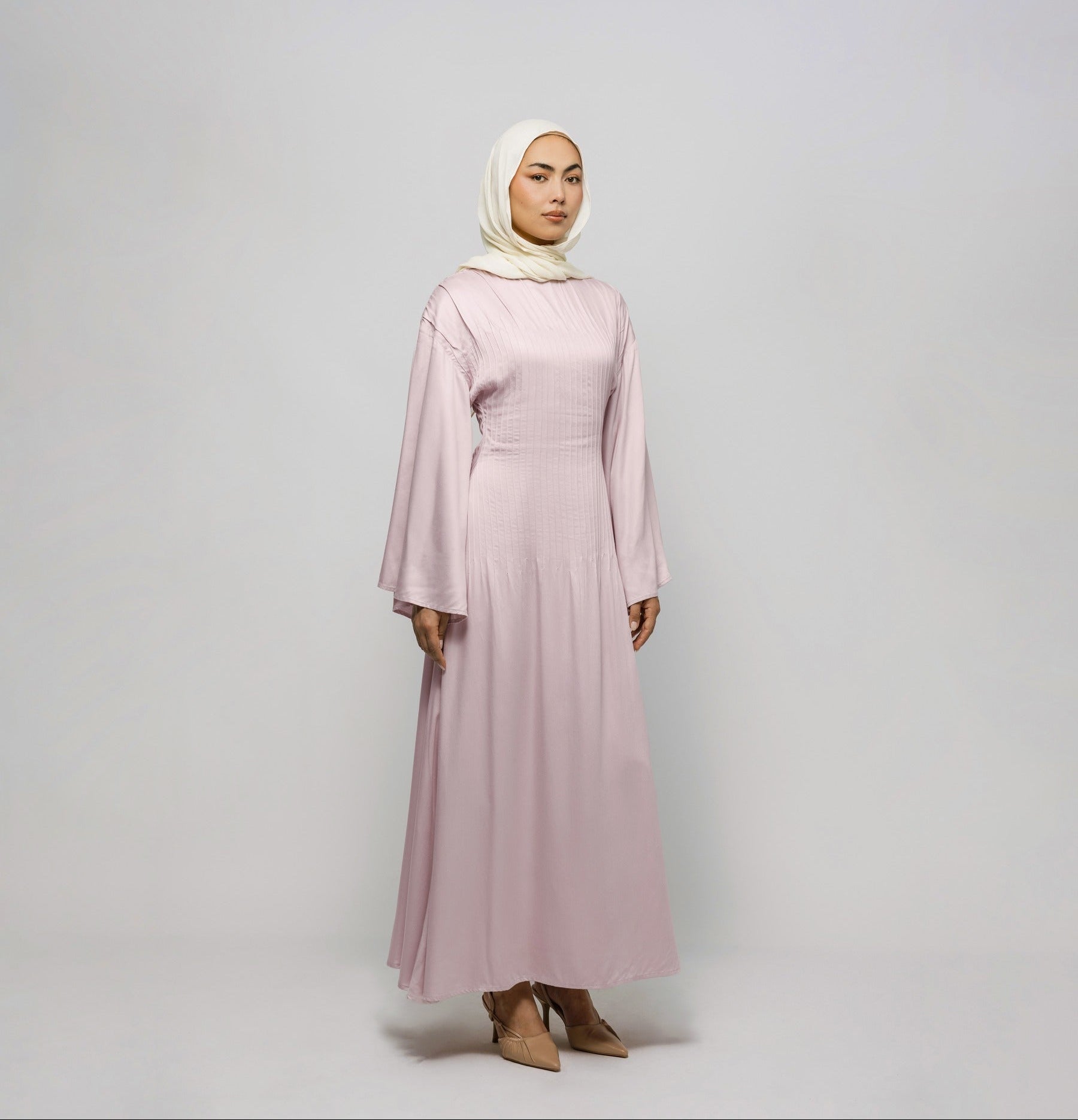Woman wearing a long pink dress and hijab on a white background