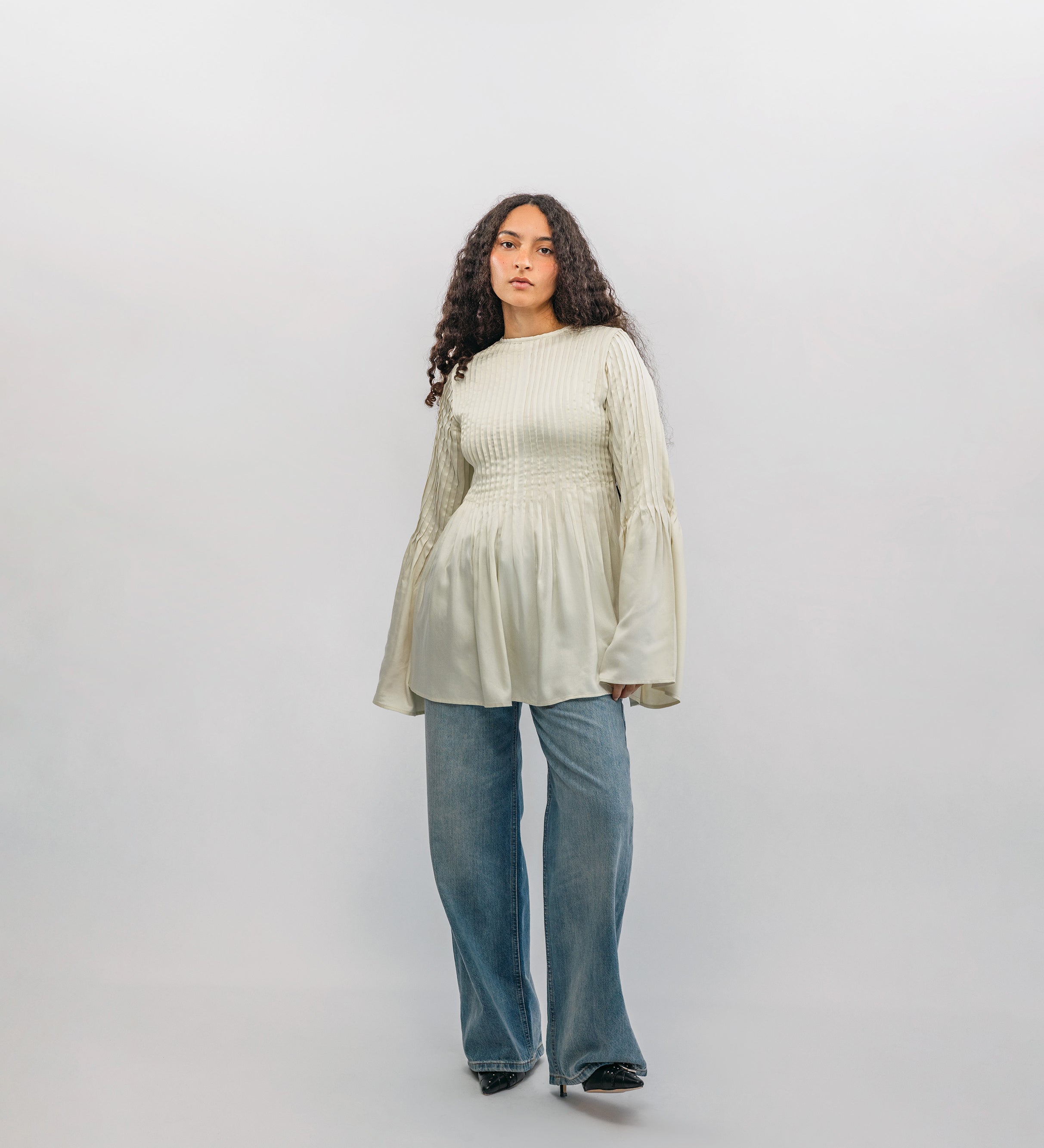 Woman wearing a light-colored blouse and blue jeans against a white background