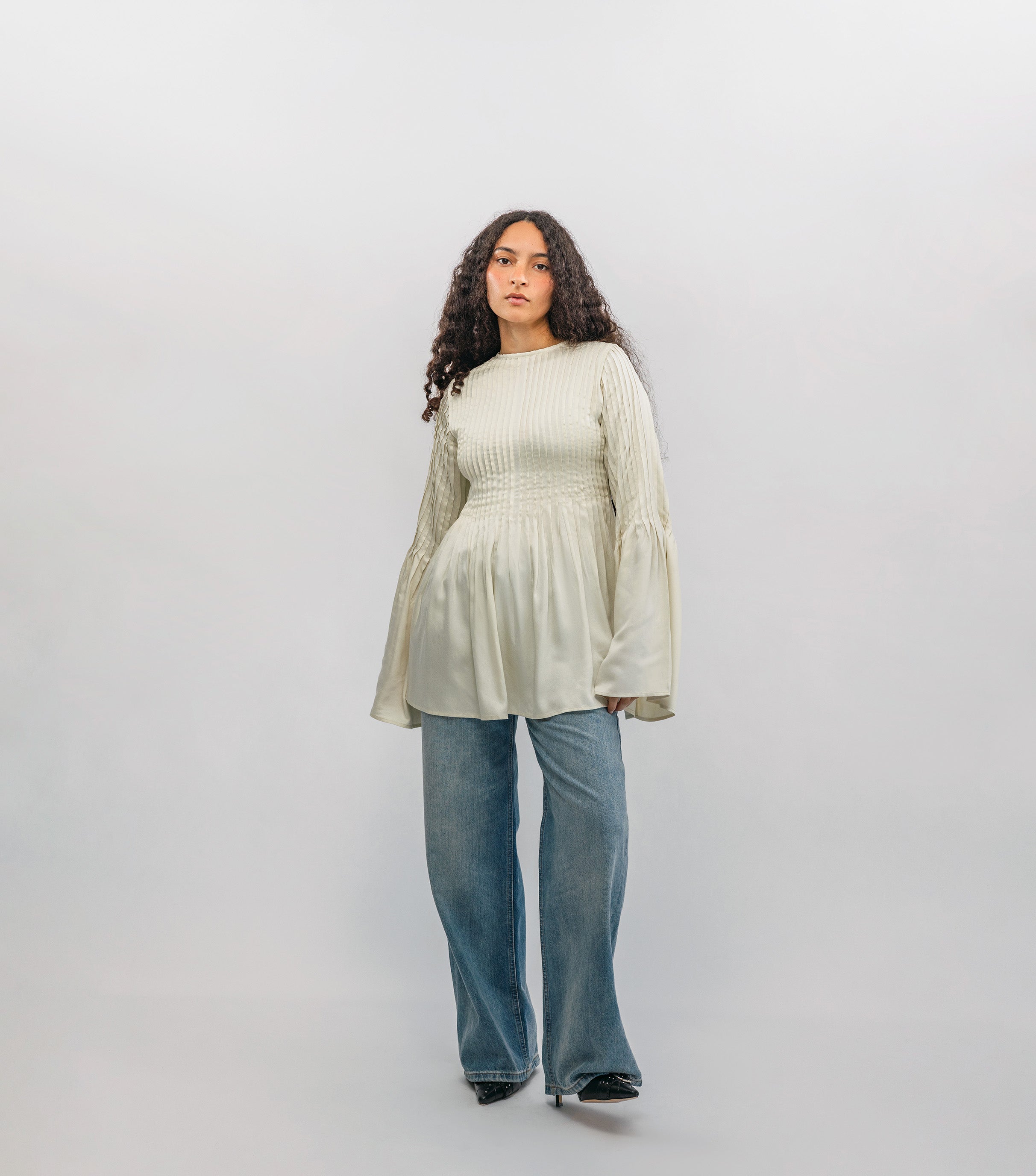 Woman wearing a light-colored blouse and blue jeans against a white background