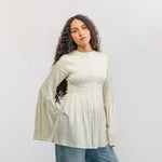 Woman wearing a light-colored blouse and blue jeans against a white background