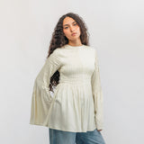 Woman wearing a light-colored blouse and blue jeans against a white background