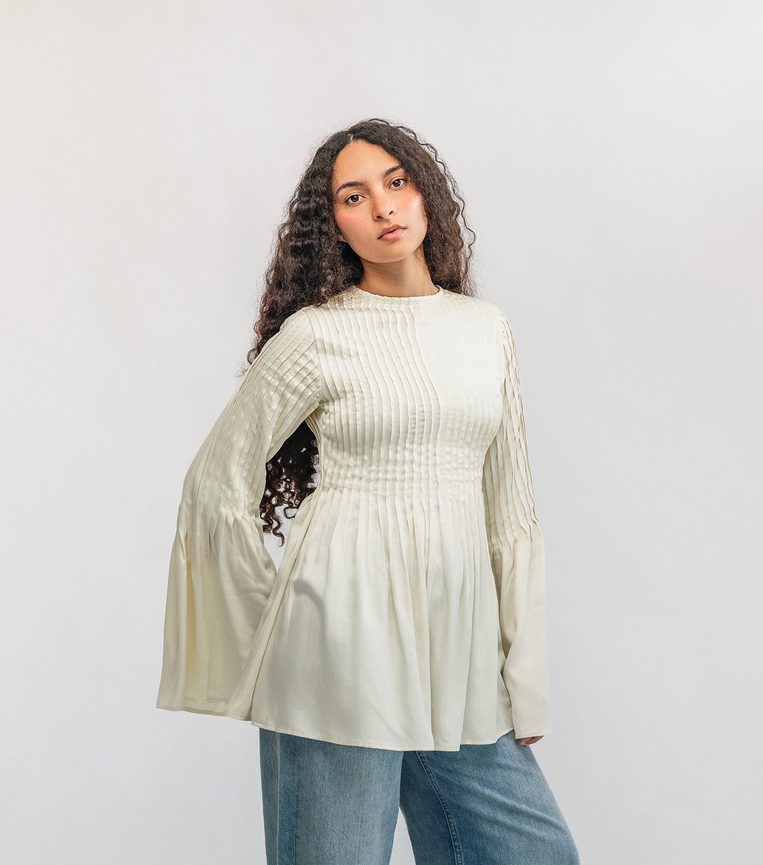 Woman wearing a light-colored blouse and blue jeans against a white background