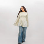 Woman wearing a light green ribbed sweater and blue jeans on a white background