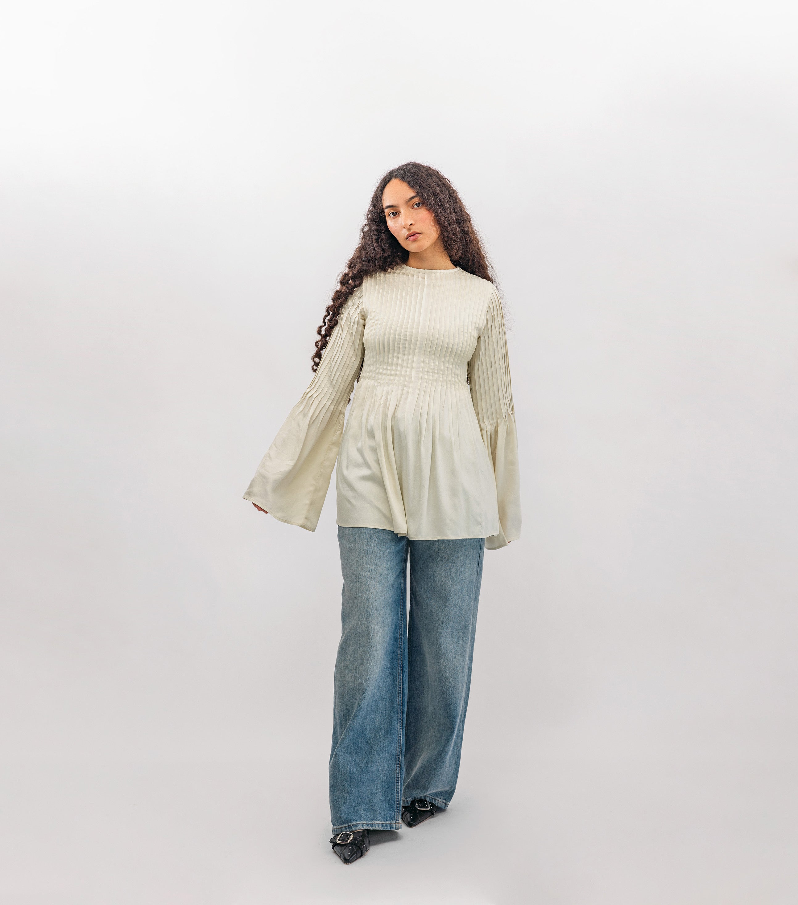 Woman wearing a light green ribbed sweater and blue jeans on a white background