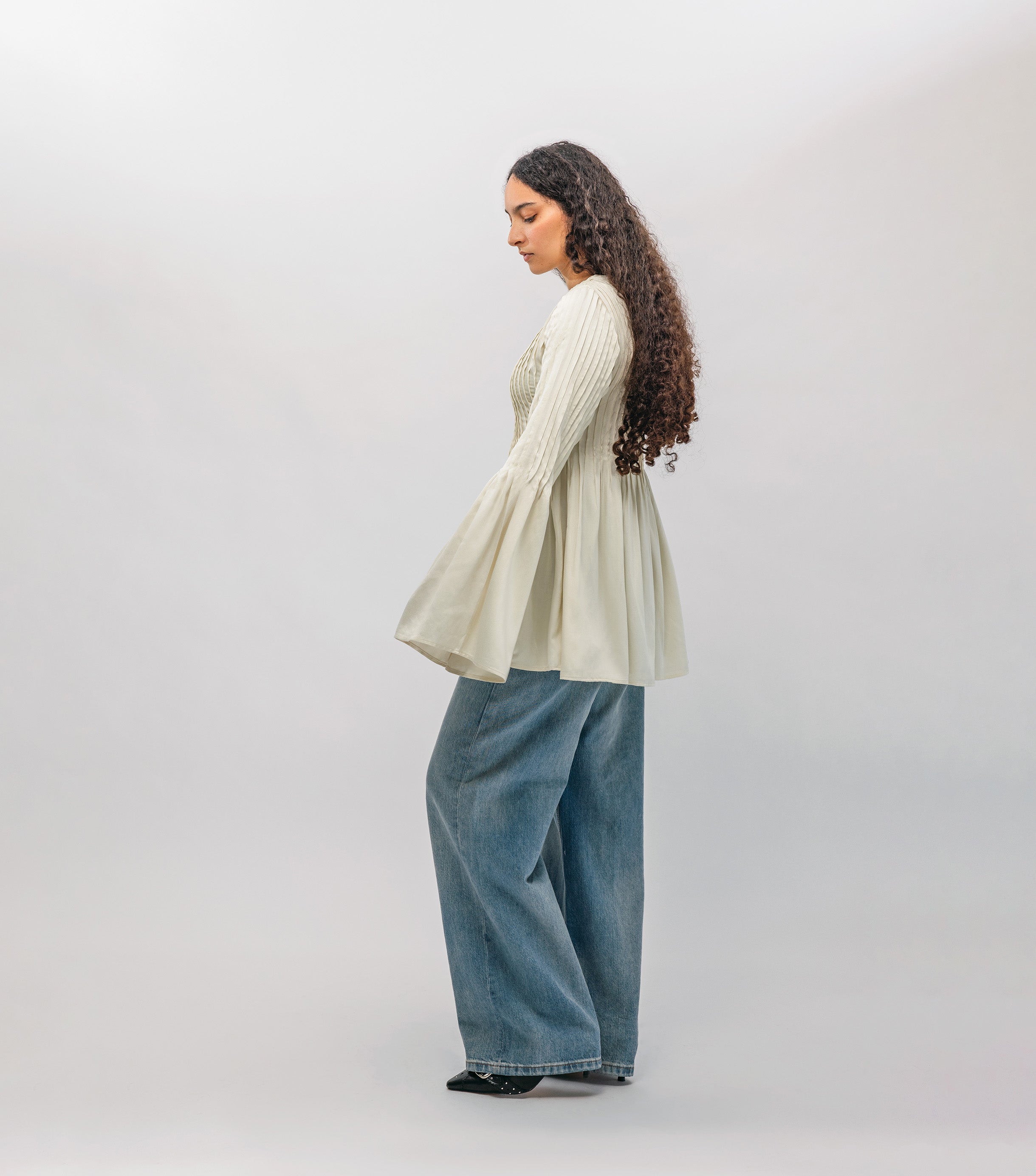 Woman wearing a light-colored sweater and blue jeans on a white background