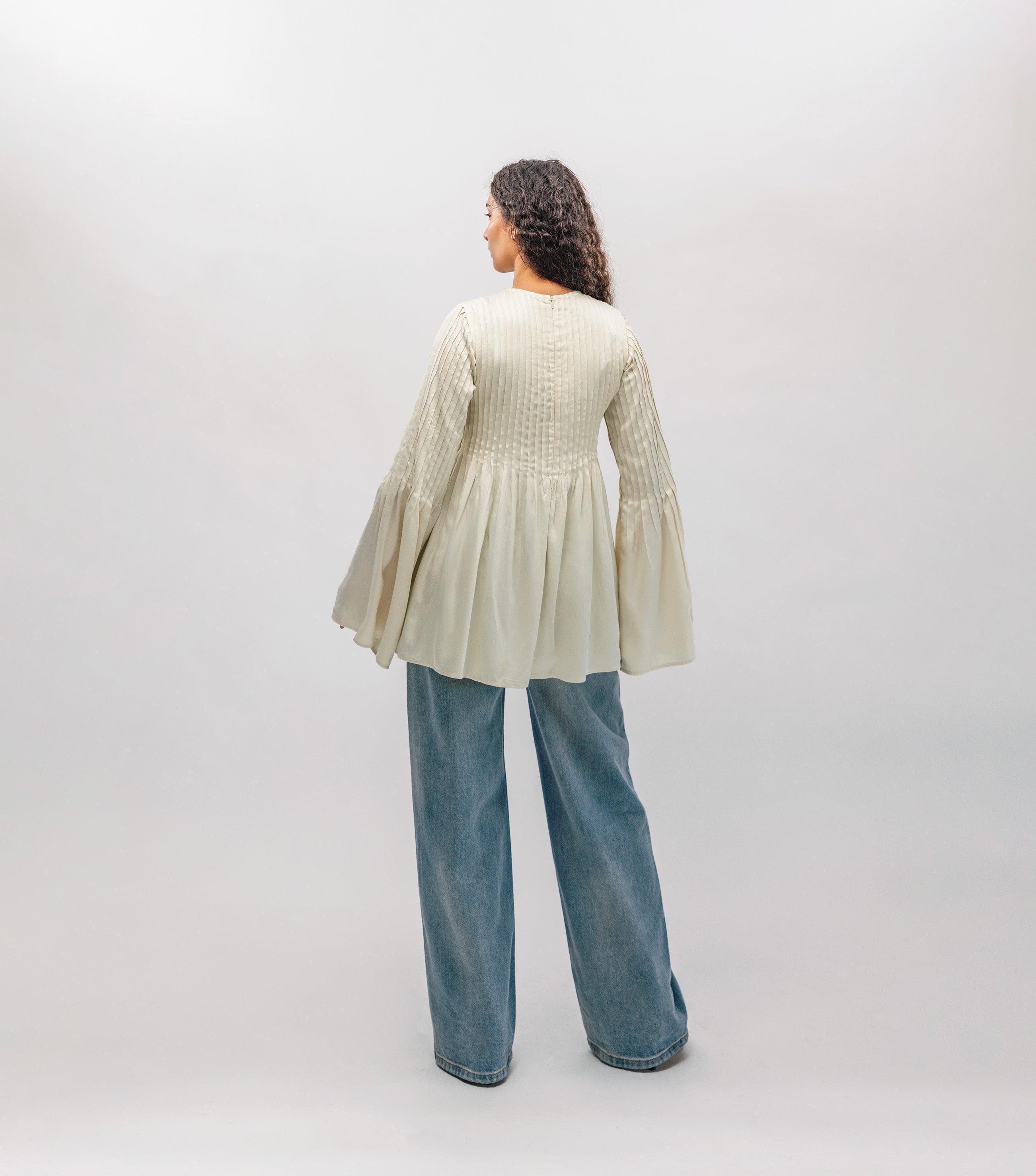 Person wearing a light-colored blouse and blue jeans against a white background