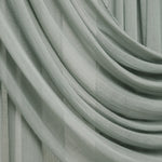 A close-up of draped sage green sheer curtains with soft folds and a light neutral background visible in the gaps.