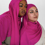 Two women wearing pink hijabs against a white background