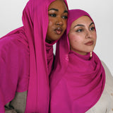 Two women wearing pink hijabs against a white background