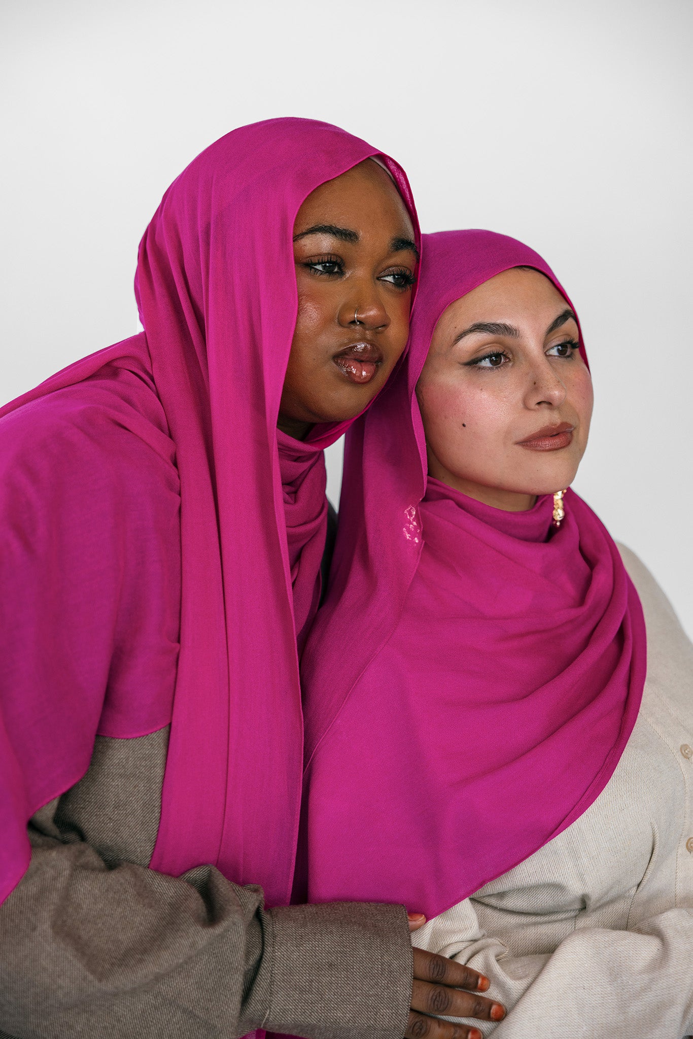 Two women wearing pink hijabs against a white background