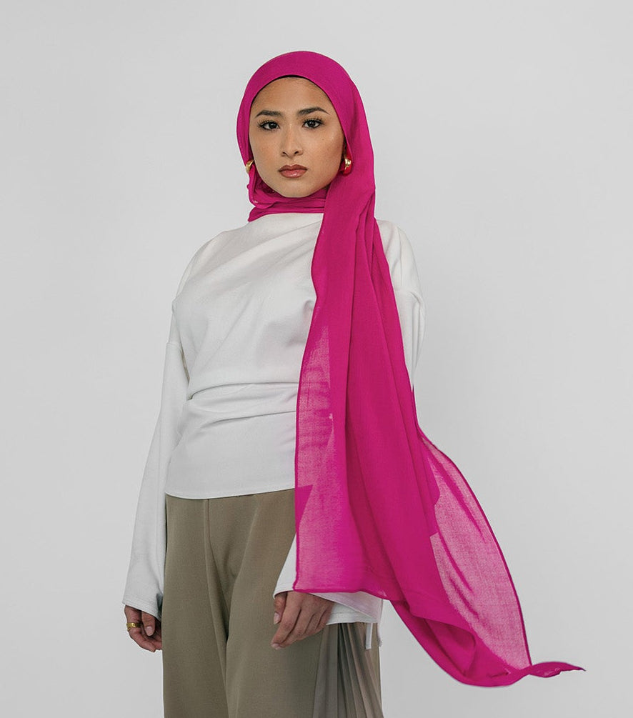Person wearing a white top and beige pants with a pink hijab on a white background