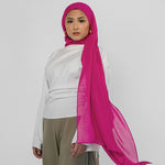 Person wearing a white top and beige pants with a pink hijab on a white background