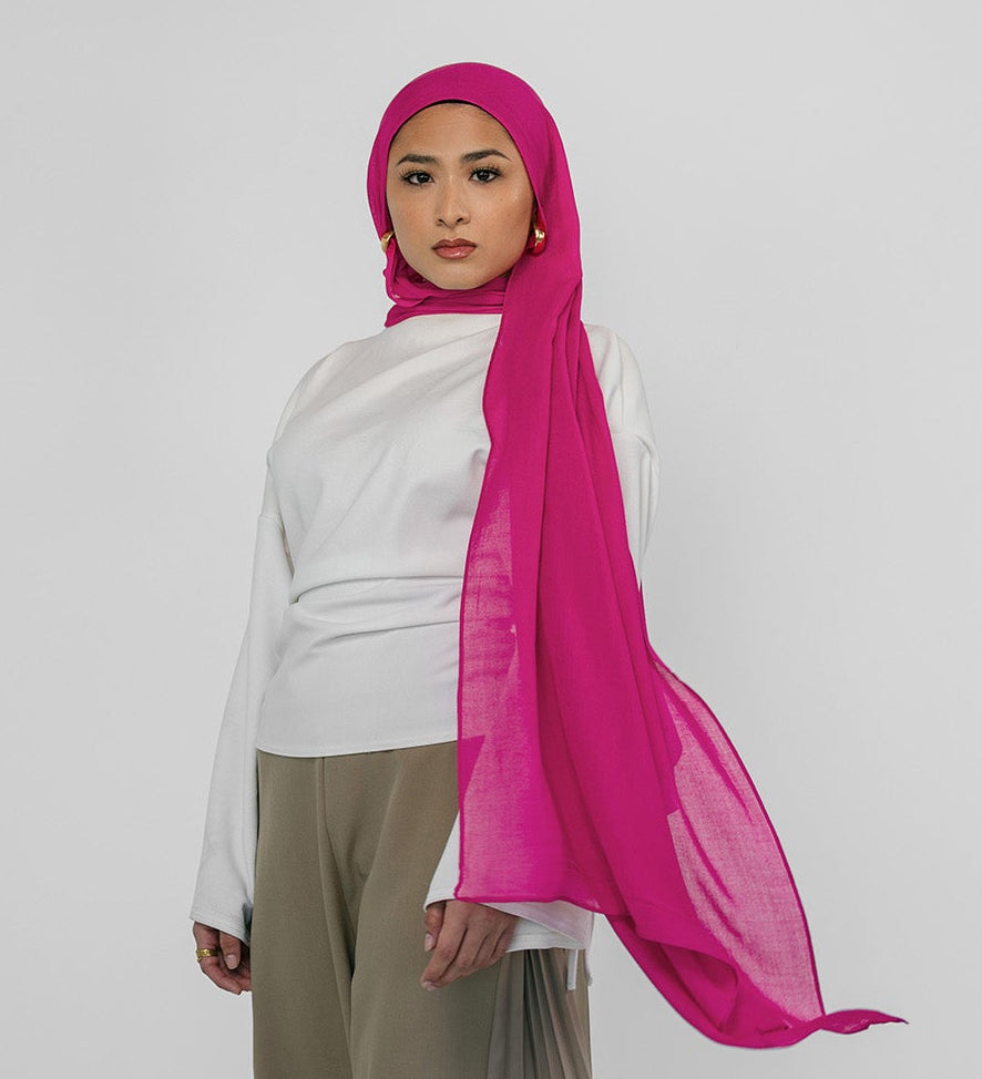 Person wearing a white top and beige pants with a pink hijab on a white background