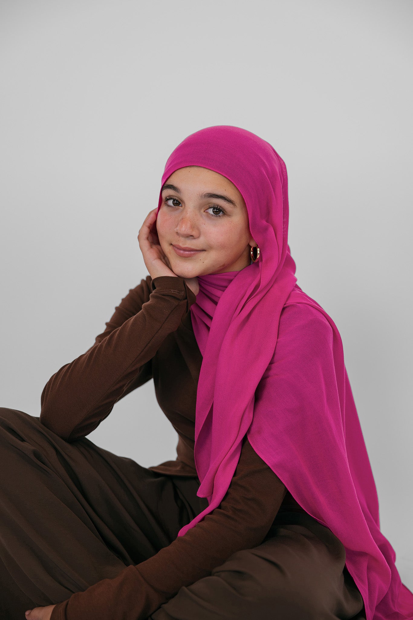 Person wearing a bright pink hijab and brown outfit on a plain background