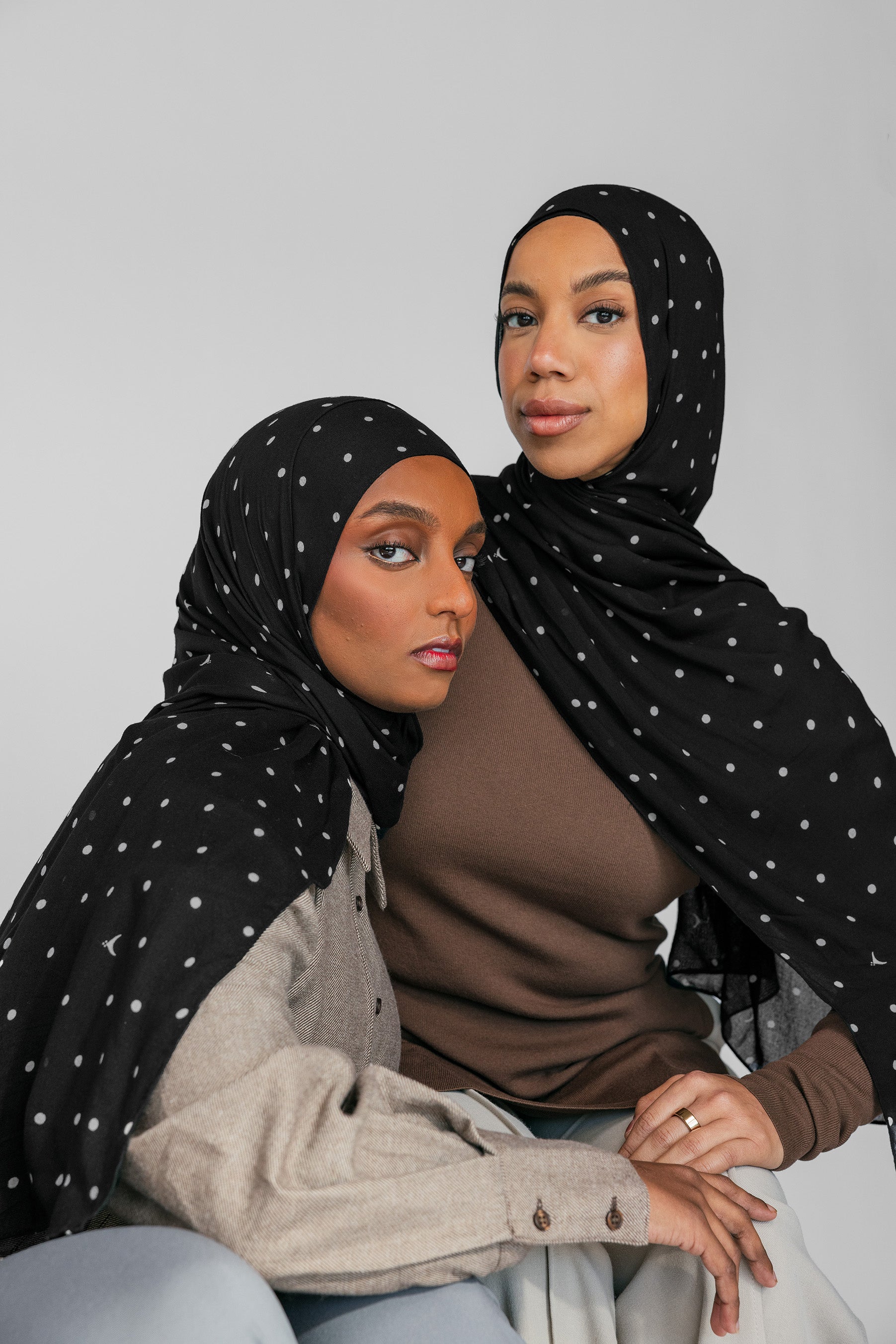 Two women wearing black hijabs with white patterns against a gray background