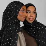 Two women wearing black polka-dot hijabs against a gray background