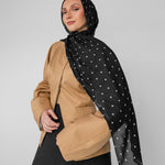 Woman wearing a black polka-dot hijab and a beige top on a gray background