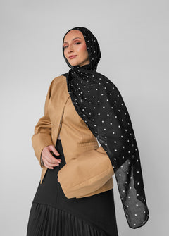 Woman wearing a black polka-dot hijab and a beige top on a gray background