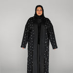 Woman wearing a black abaya with white embellishments on a gray background