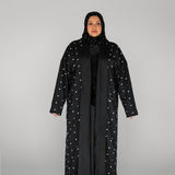 Woman wearing a black abaya with white embellishments on a gray background