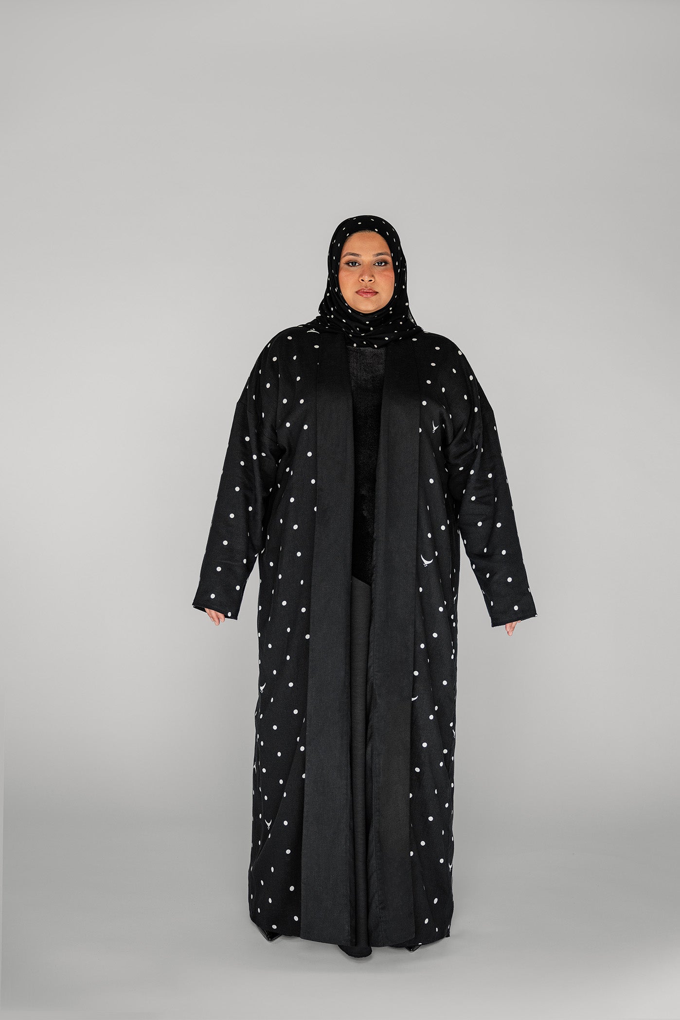 Woman wearing a black abaya with white embellishments on a gray background