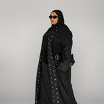 Woman wearing a black abaya with white polka dots on a gray background