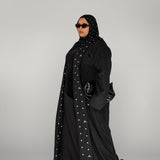 Woman wearing a black abaya with white polka dots on a gray background