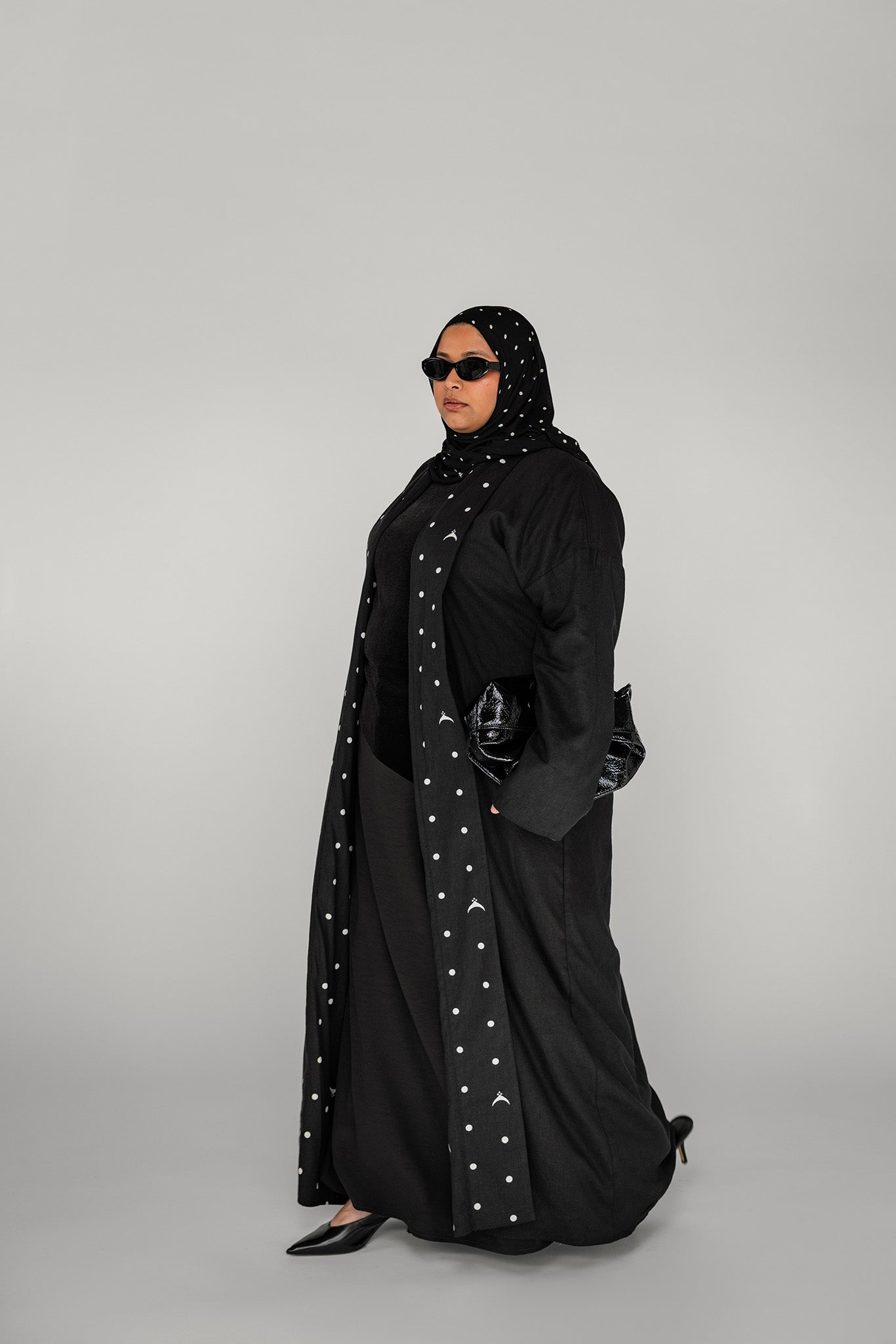 Woman wearing a black abaya with white polka dots on a gray background