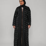 Person wearing a black abaya with white polka dots on a gray background