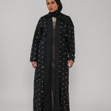 Person wearing a black abaya with white polka dots on a gray background