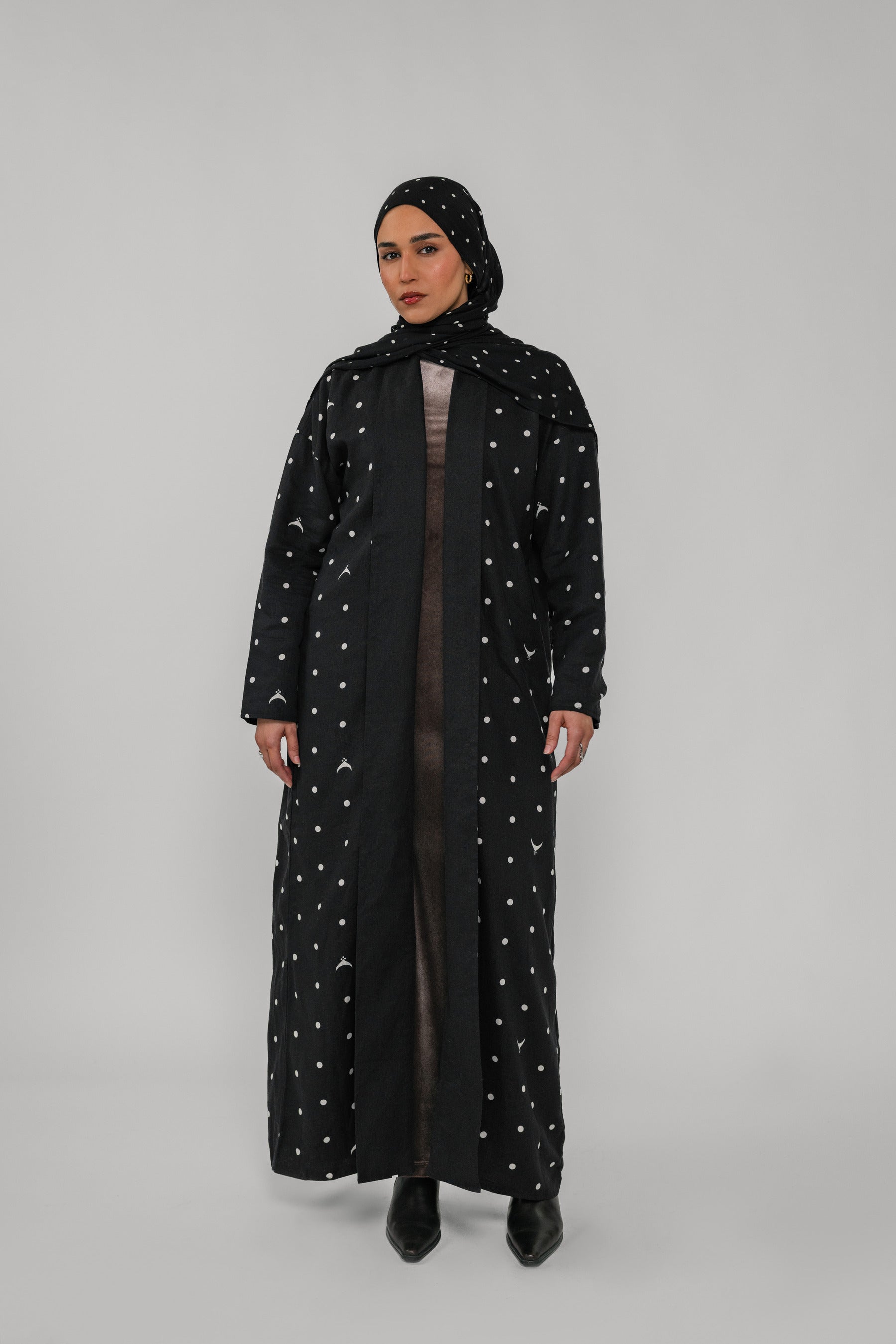 Person wearing a black abaya with white polka dots on a gray background