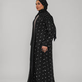 Woman wearing a black abaya with white patterns on a gray background