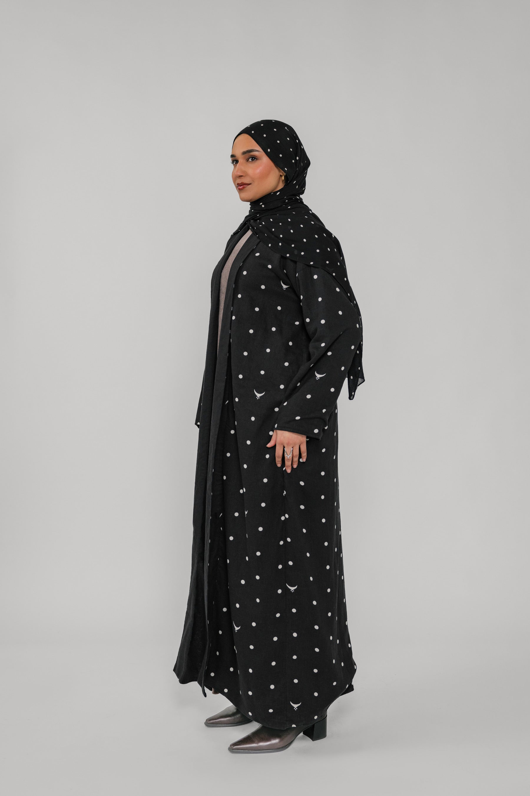 Woman wearing a black abaya with white patterns on a gray background