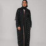 Woman wearing a black abaya with polka dot patterns on a gray background