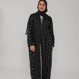 Woman wearing a black abaya with polka dot patterns on a gray background