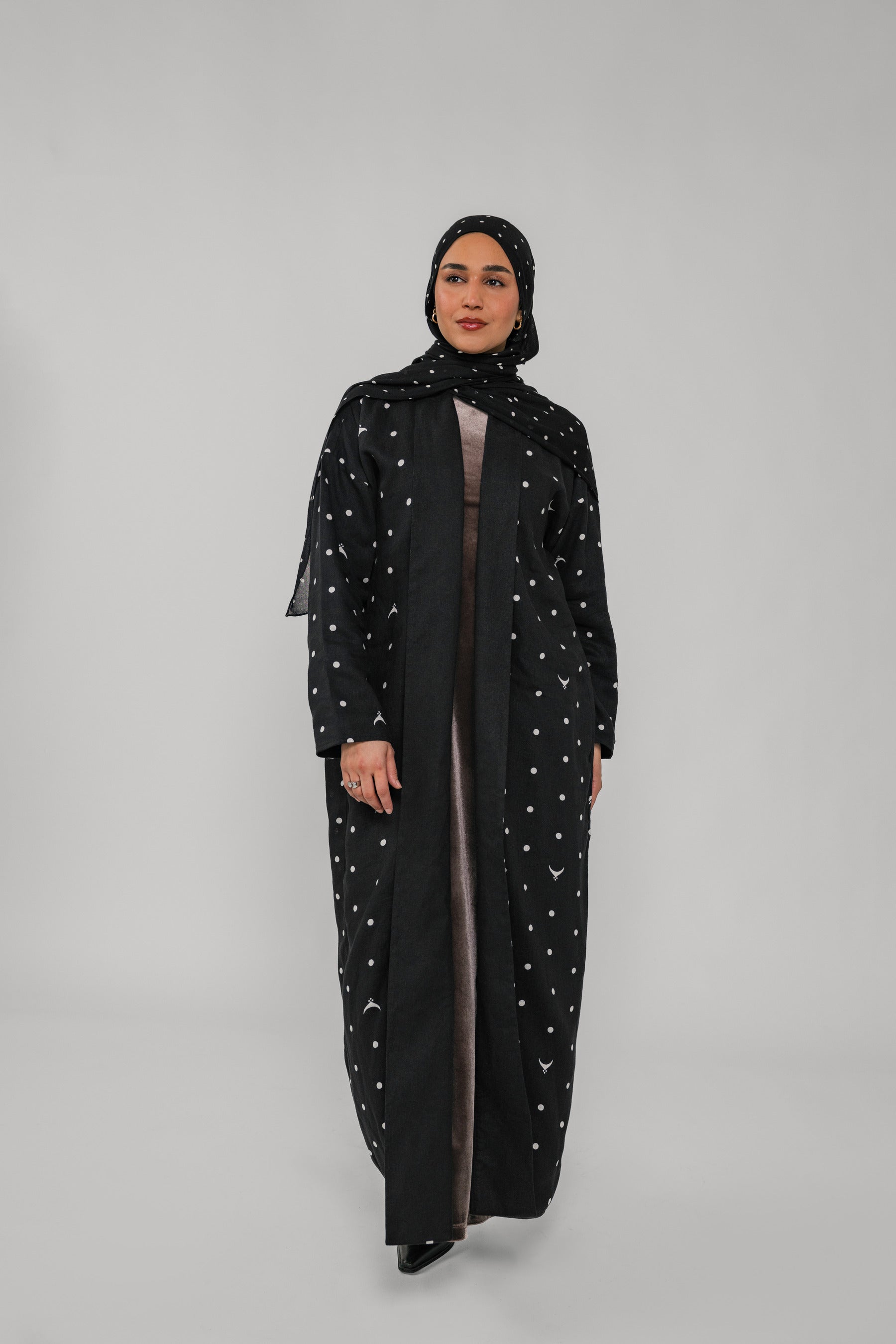 Woman wearing a black abaya with polka dot patterns on a gray background