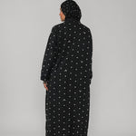Person wearing a black abaya with white patterns on a gray background