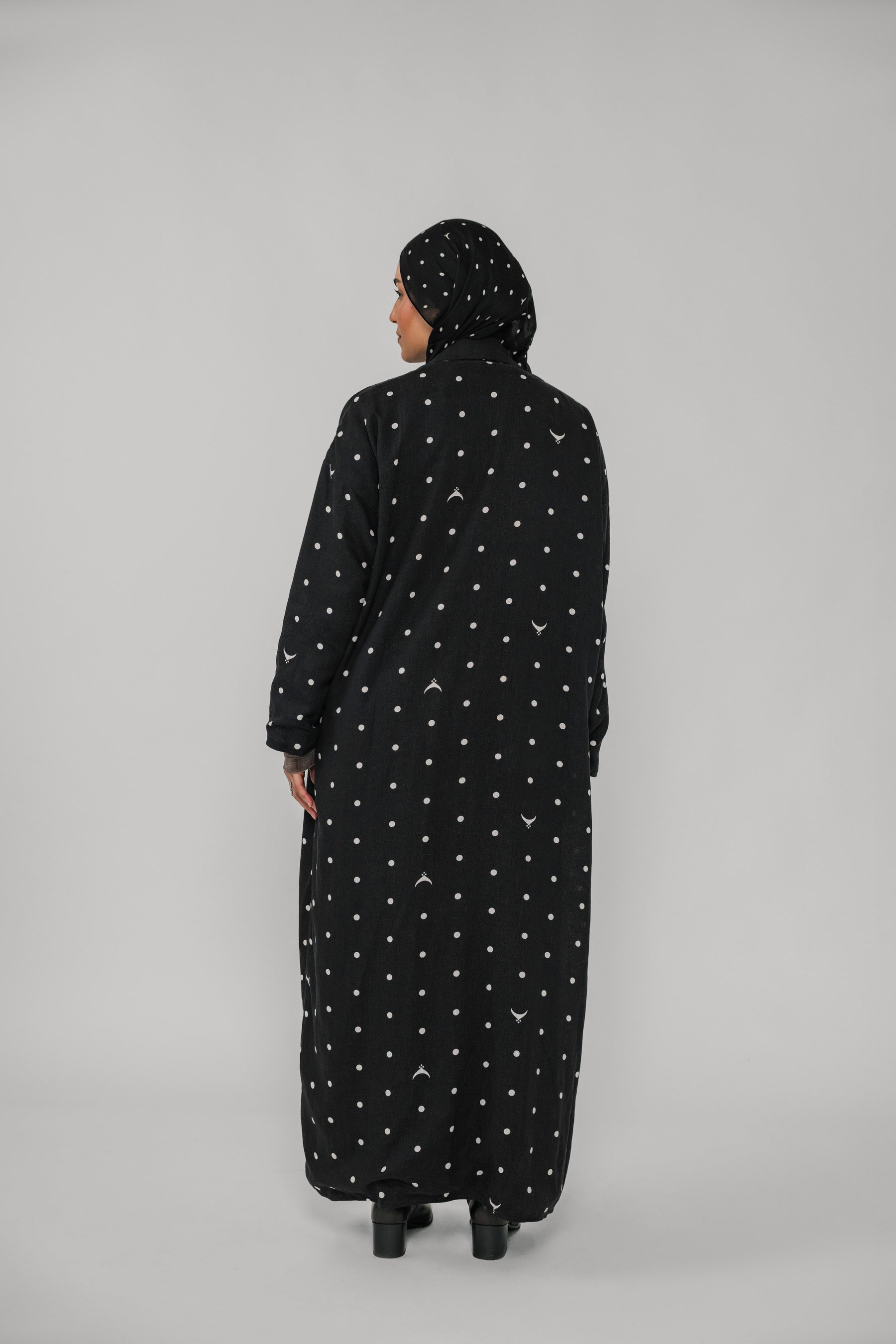 Person wearing a black abaya with white patterns on a gray background