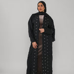 Woman wearing a black abaya with polka dot details on a gray background