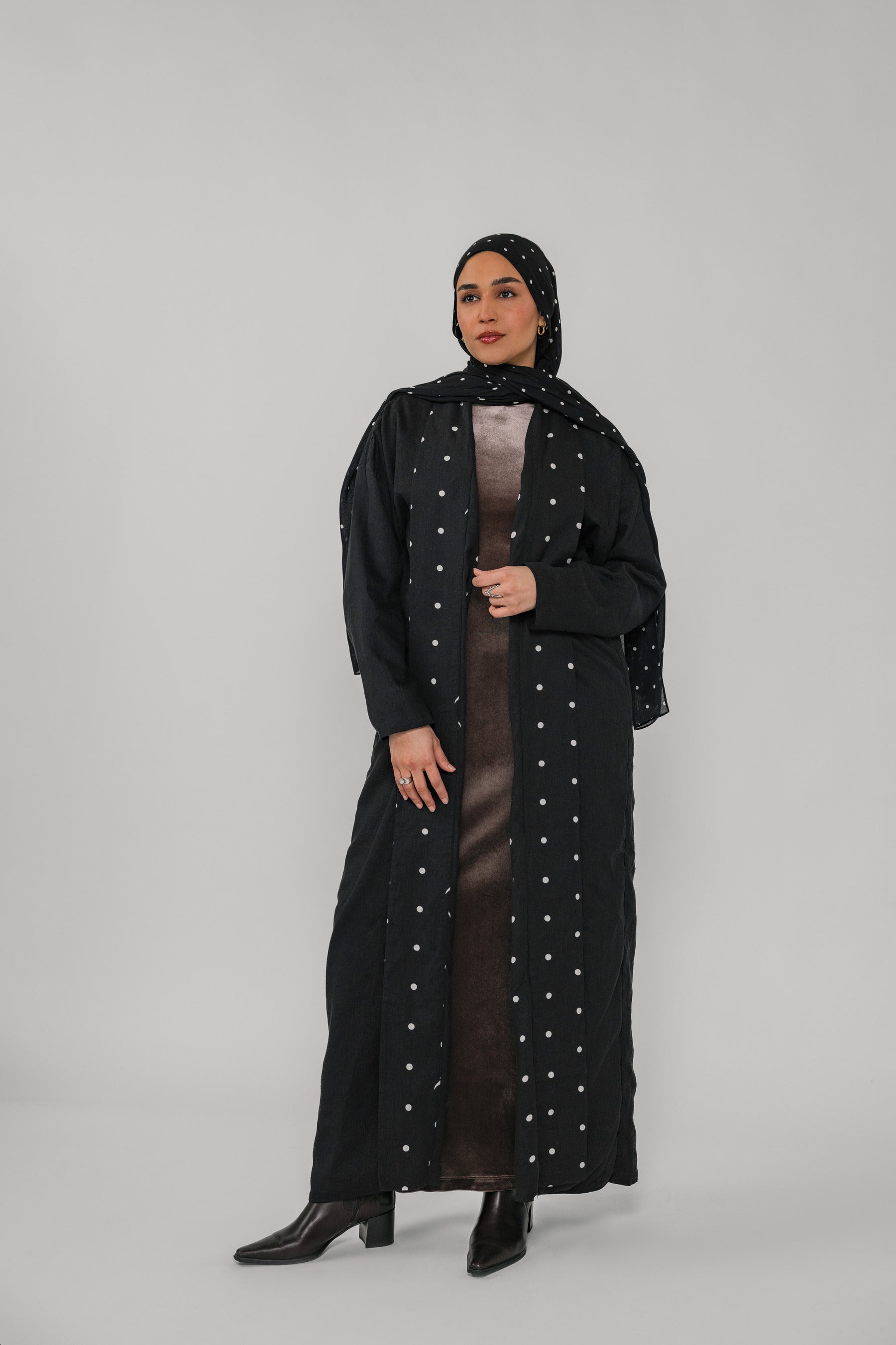 Woman wearing a black abaya with polka dot details on a gray background