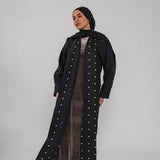 Woman wearing a long black coat with white polka dots and a matching headscarf on a gray background