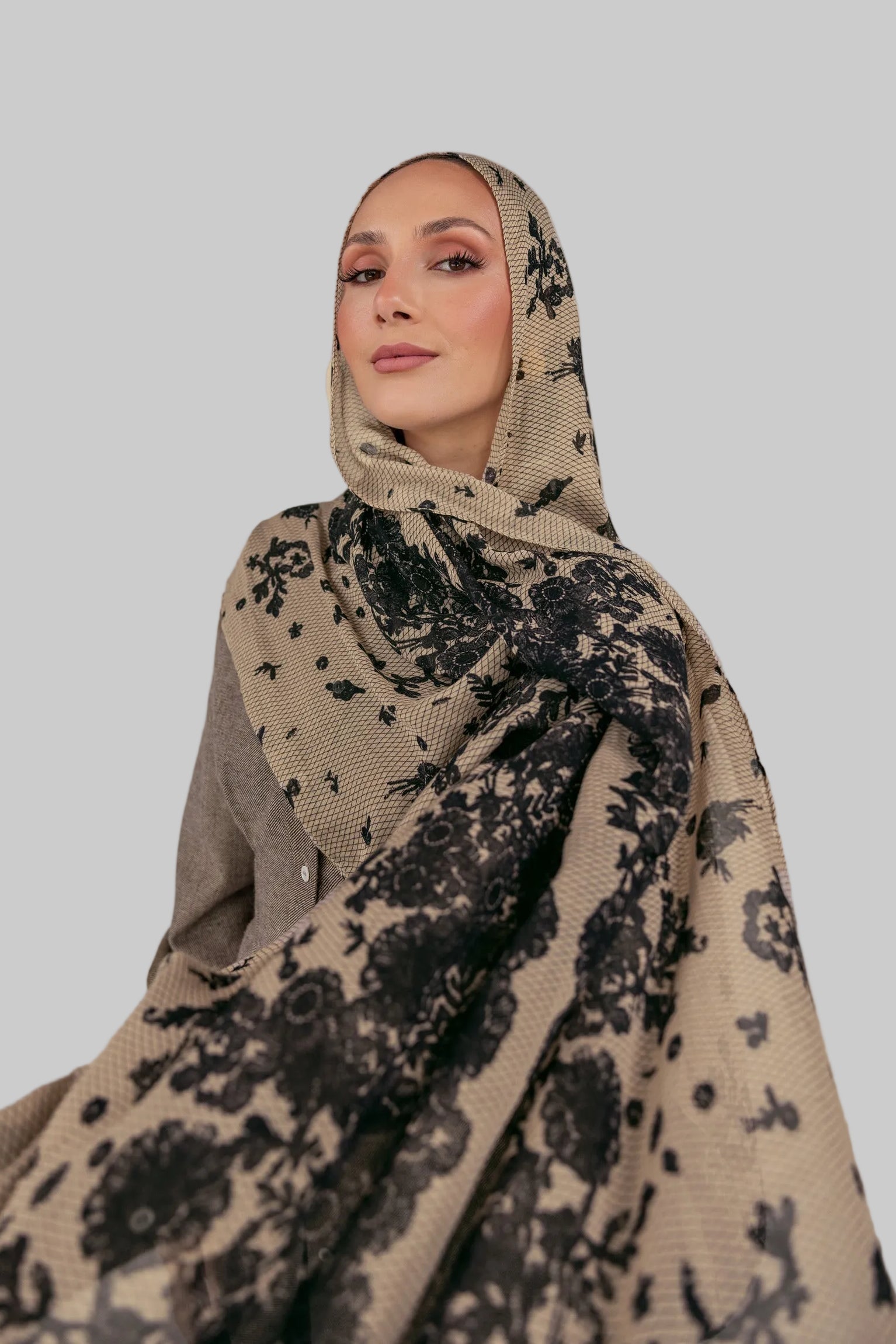 Woman wearing a beige hijab with black floral patterns against a white backdrop.