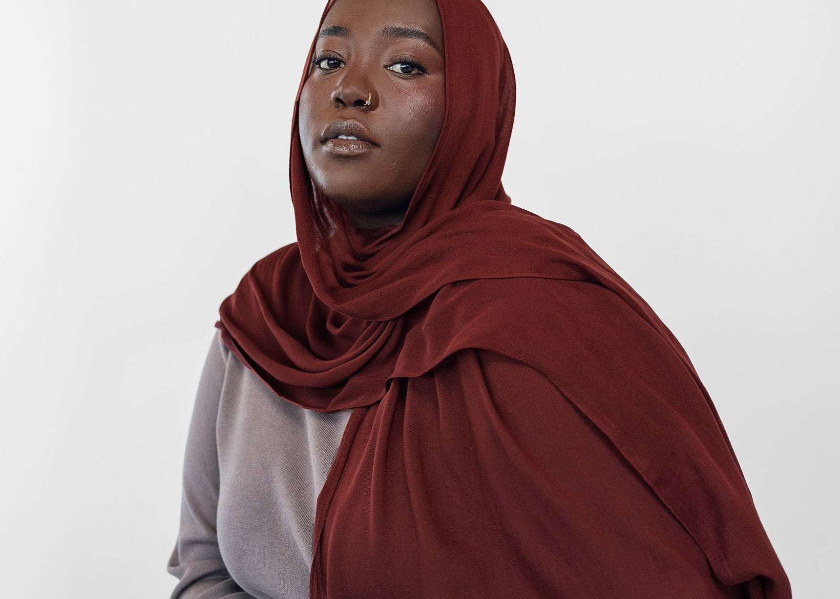 Woman wearing a red hijab and dark pants against a white background