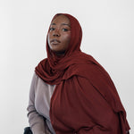 Woman wearing a red hijab and dark pants against a white background