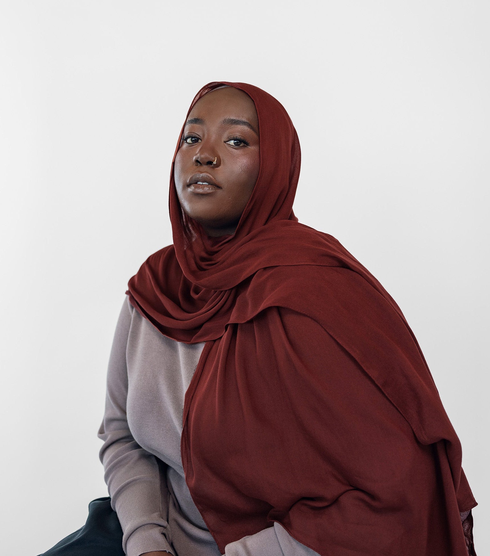 Woman wearing a red hijab and dark pants against a white background